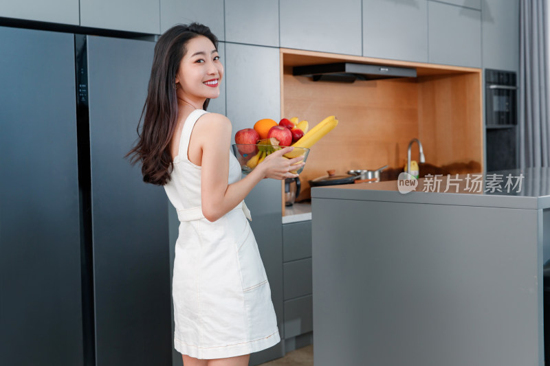 拿着水果的青年女人站在冰箱前