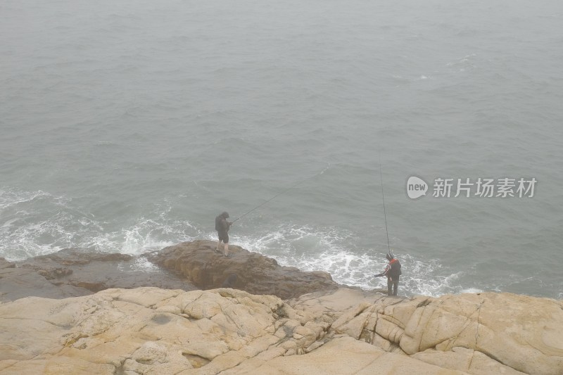 海边岩石上两人垂钓的场景