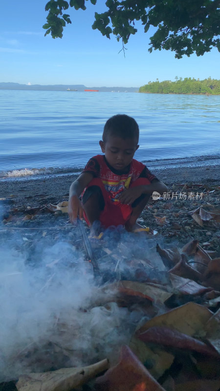 印尼当地小男孩在海边沙滩上生火