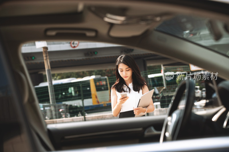 低头使用手机的青年女人走向汽车