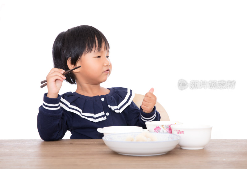 白背景前的餐桌上边吃饭边玩耍的中国小姑娘