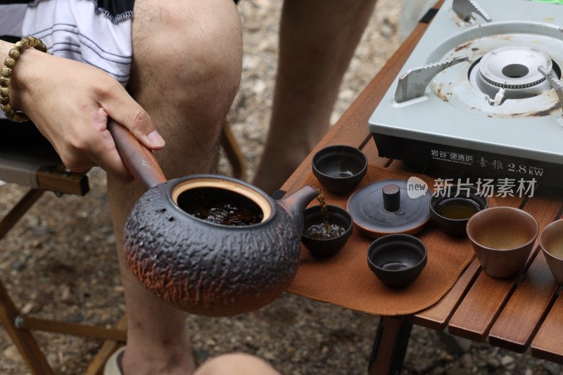 户外露营时用陶制茶壶倒茶的场景