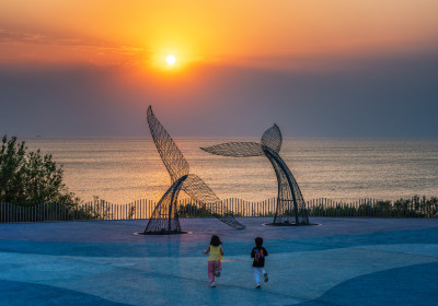 两名儿童奔向夕阳下的大海与雕塑