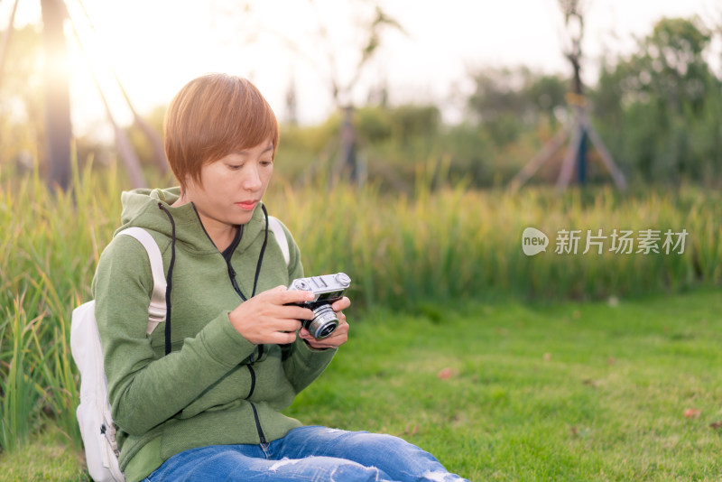 年轻的女性坐在公园草地上使用老式相机