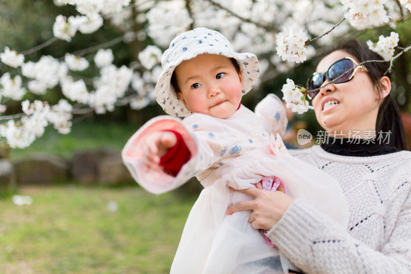 快乐年轻亚洲母亲抱着可爱小女儿看美丽樱花