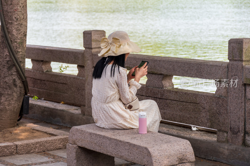 女子湖边石凳上使用手机