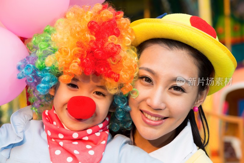 年轻妈妈和扮成小丑的女儿在游乐园玩