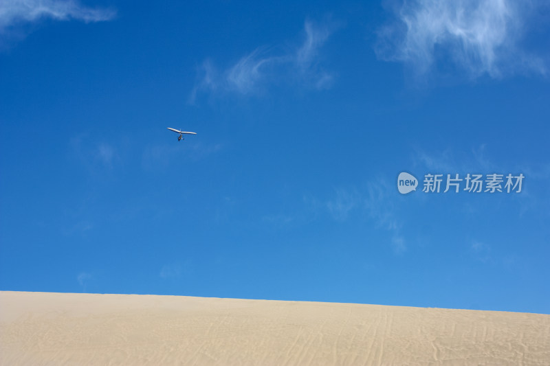 蓝天白云滑翔机从沙丘上飞过