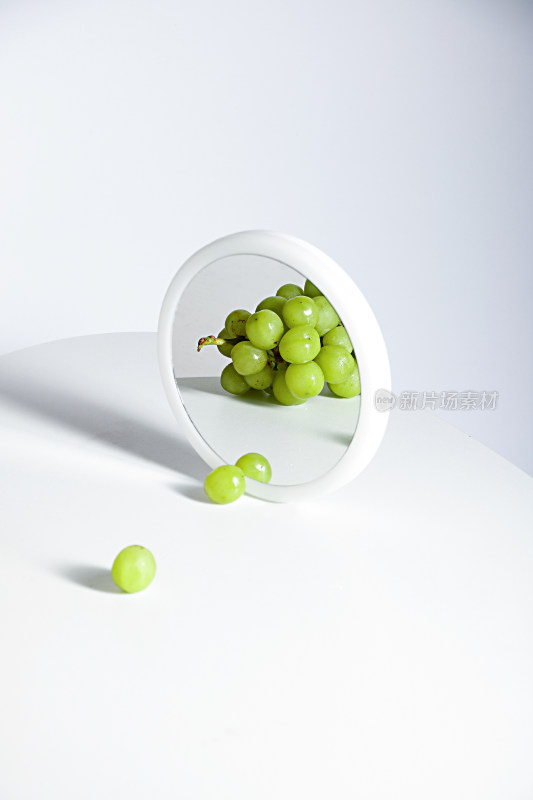 白色桌面和镜子中的新鲜水果葡萄提子