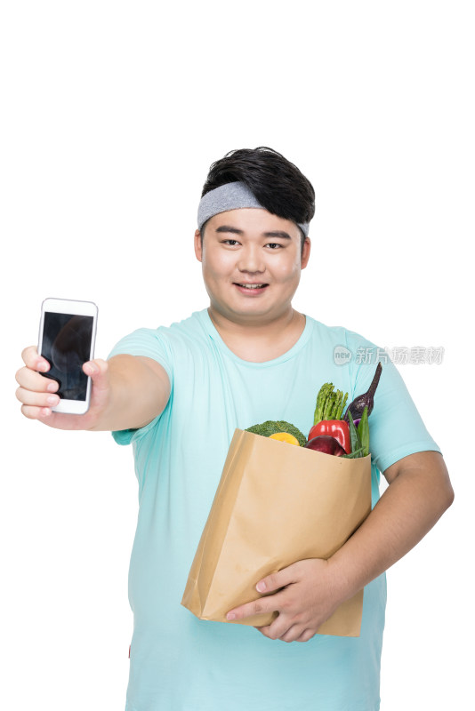 肥胖的年轻男子拿着手机和各种蔬菜