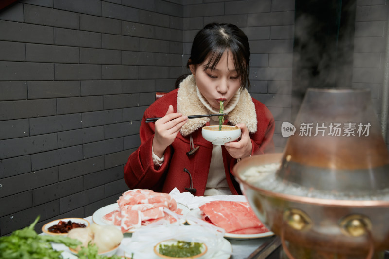 在饭店吃传统铜锅涮肉的亚洲少女