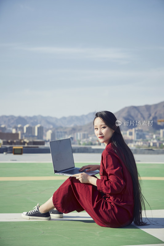 亚洲商务年轻女性在楼顶停机坪使用电脑办公