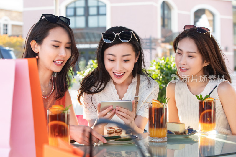 年轻女孩们坐在露天咖啡馆看手机视频