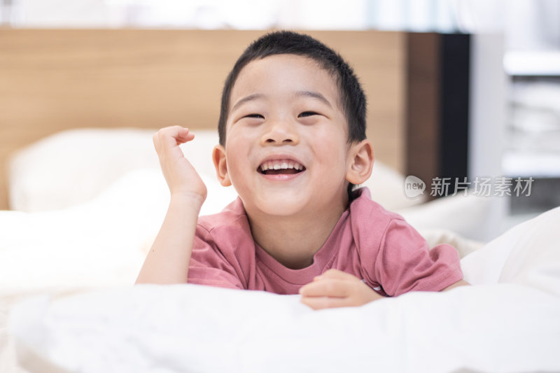 一个小男孩趴在床上看镜头微笑