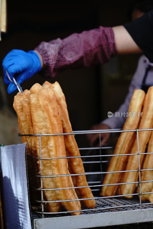 戴手套的手夹起金属架上的油条