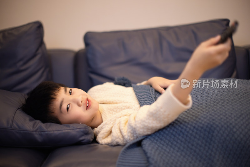 一个中国小男孩躺在沙发上玩遥控器