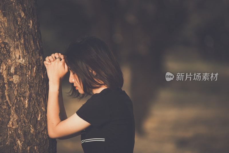 女子倚树双手抱头神情低落