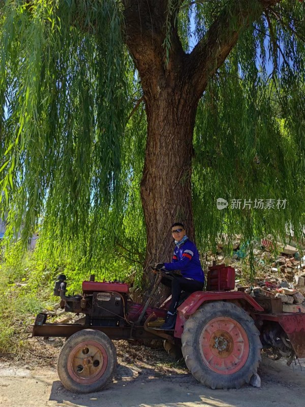 男子坐在大树下的拖拉机上休息