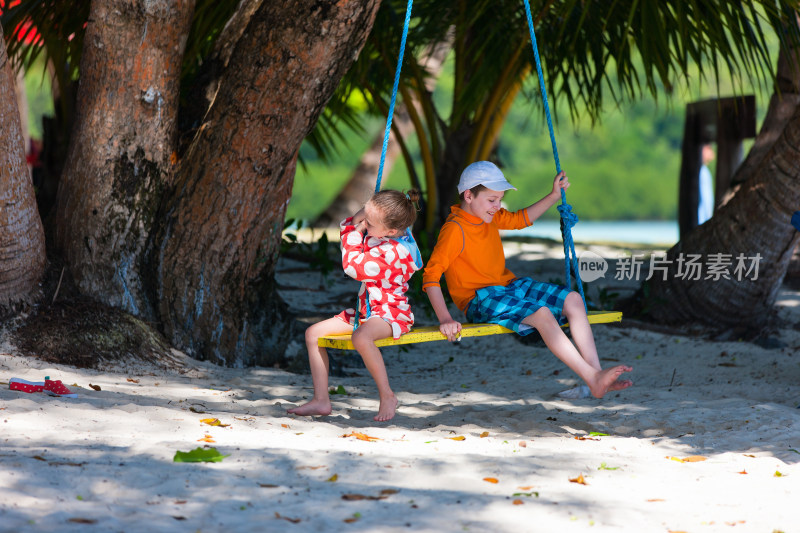 沙滩上两个孩子坐秋千玩耍