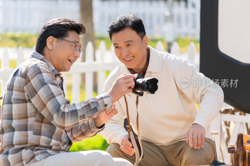 两个老年男人坐在露营地看数码相机