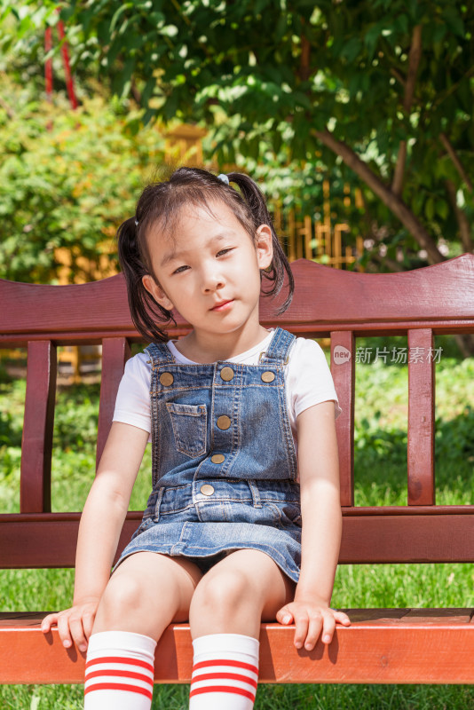 小女孩穿着背带裤坐在公园长椅上