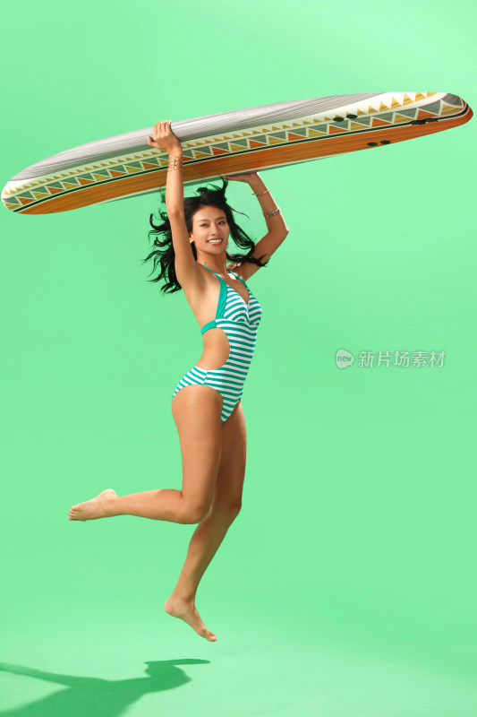 穿泳装的美女举着冲浪板跳跃