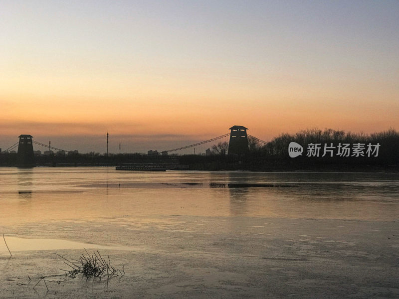 暮色下结冰河面及吊桥的静谧风景