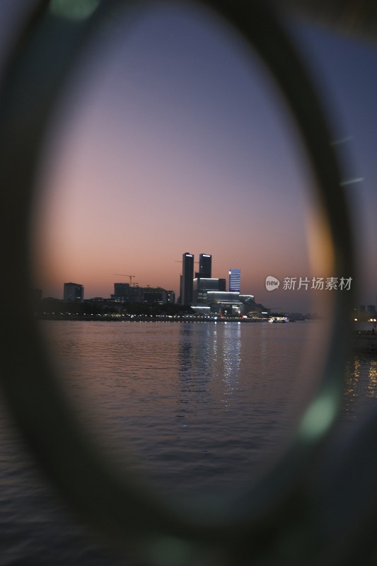 透过圆孔拍摄的江边城市暮色夜景