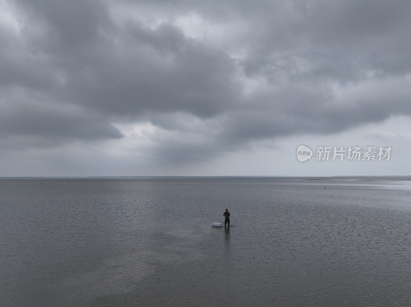 乌云笼罩下的水域中一人独自站立