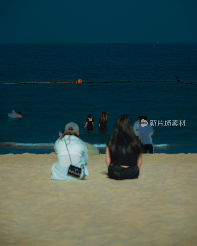 夜晚坐在海滩上吹风的人们背影