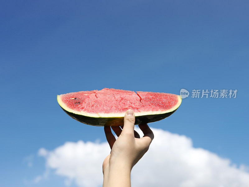 在蓝天白云的背景中，手拿着夏日水果西瓜