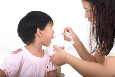 白背景前年轻妈妈正在给孩子喂饭