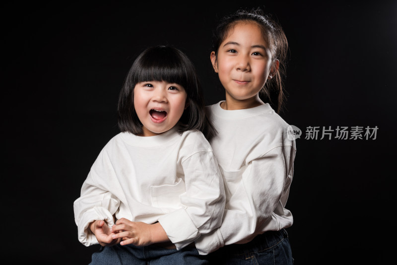 坐在黑背景前玩耍的两个亚裔女孩