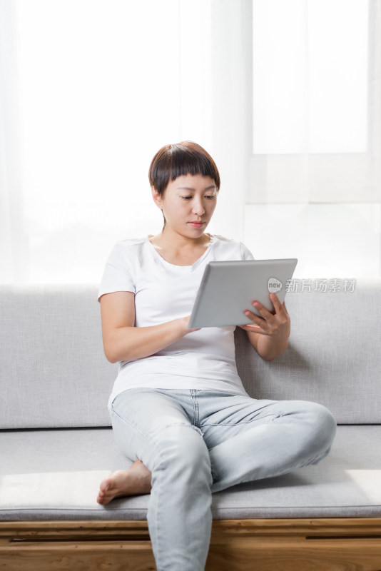 中国女性坐在沙发上使用平板电脑
