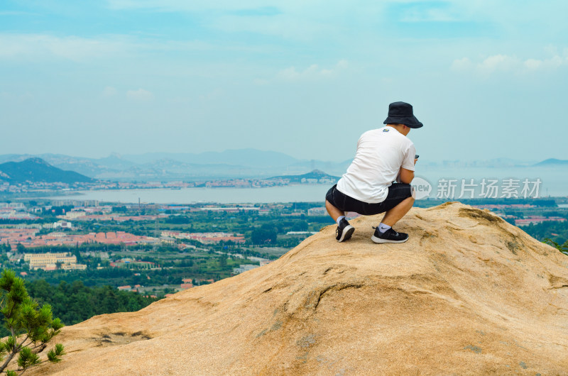 一个登上山顶后，往下望的男性年轻人背影