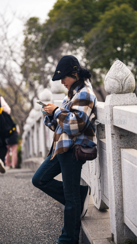 户外倚栏女子低头看手机