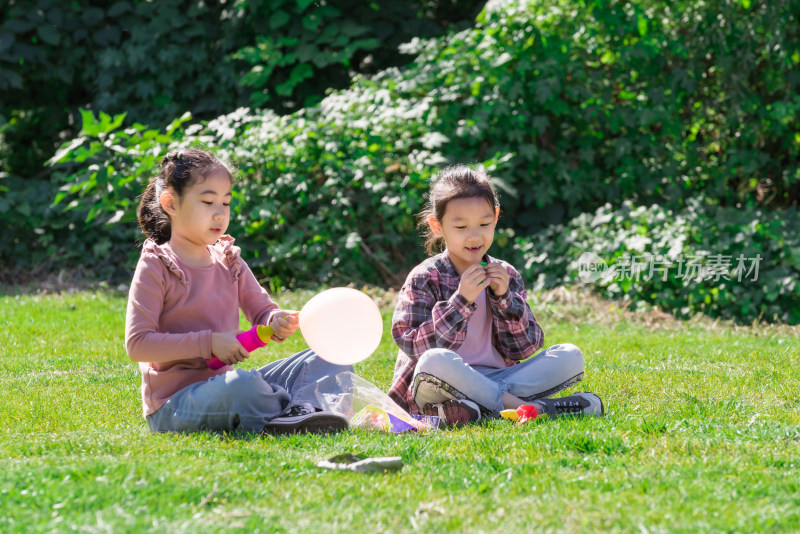秋天午后两个坐在草坪上玩气球的女孩