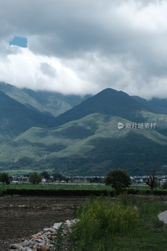 阴云下的青山远景及山脚下的土地