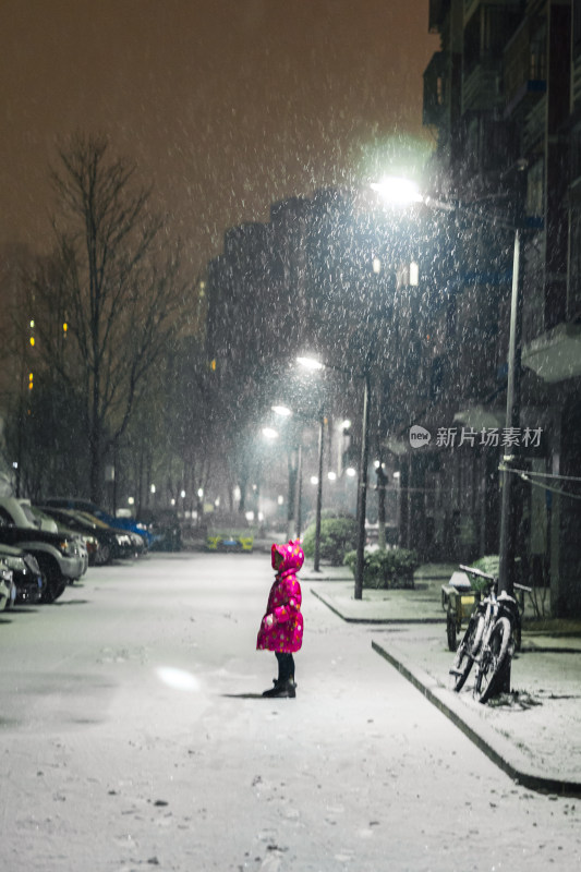 雪中穿着红衣的小女孩站在街道上