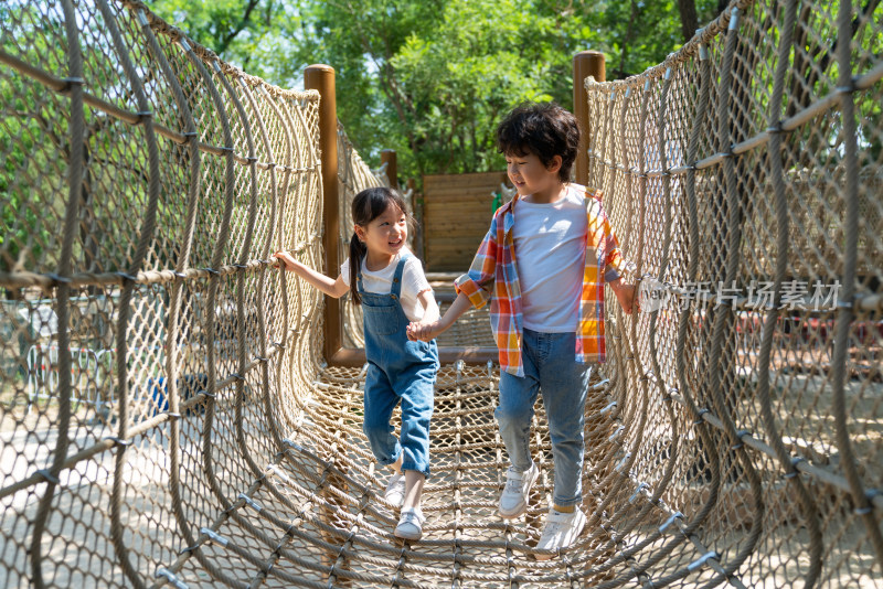 两个小孩子相互鼓励牵手走绳桥