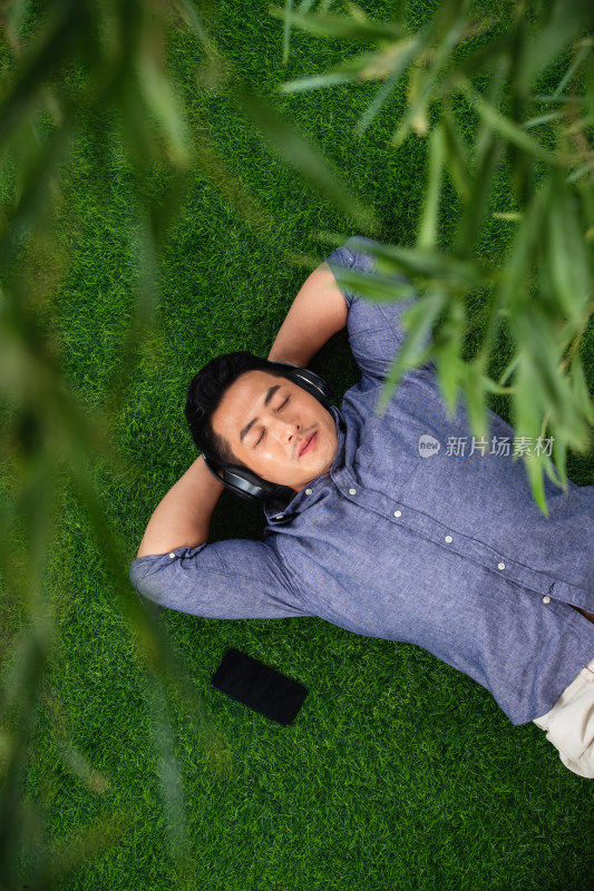 躺在草地上听音乐的青年男人