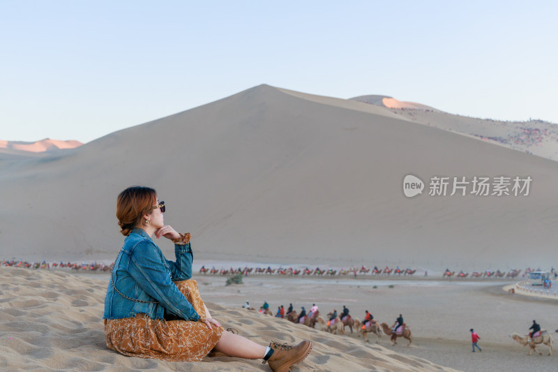 女子坐沙漠观景骆驼队穿行