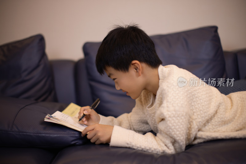 一个中国小男孩趴在沙发上做作业