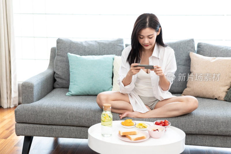 年轻女士坐在沙发上玩手机游戏