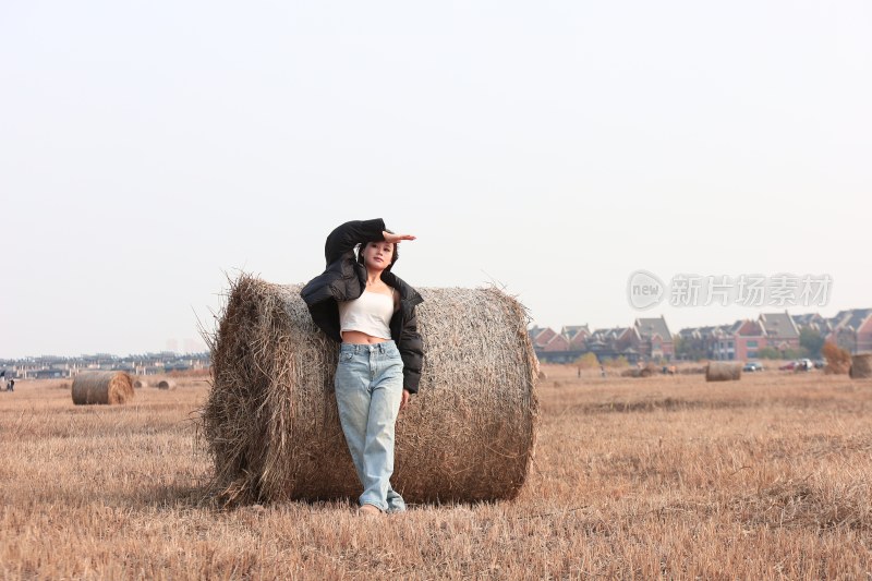 女子倚靠草垛于田野摆姿