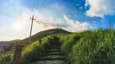 蓝天白云下绿草丛生的登山路