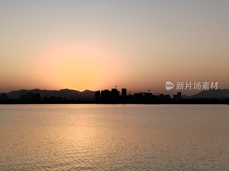 夕阳下的城市剪影与平静水面相映成趣