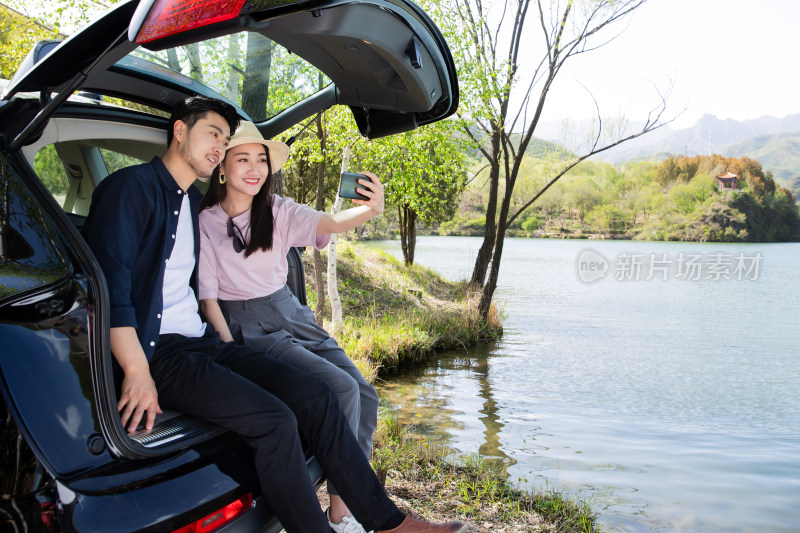 青年夫妇坐在汽车后备箱里拍照