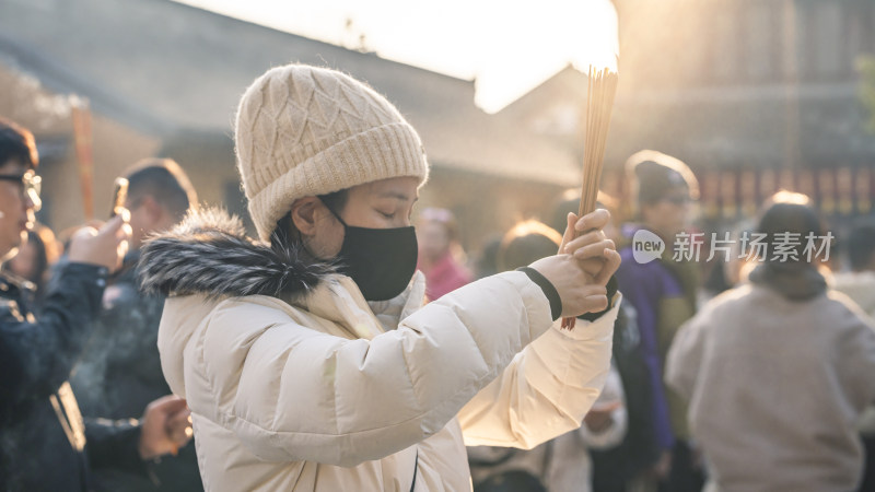 戴帽女子手持香烛神情专注似在祈福