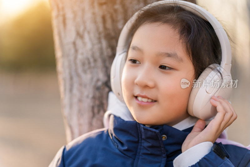 冬日暖阳在公园树林中带耳机欣赏音乐的女孩